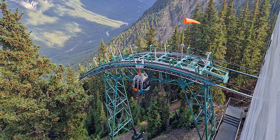 The Banff Gondola hangs above a steep drop, surrounded by the dramatic tree line of Banff National Park. 