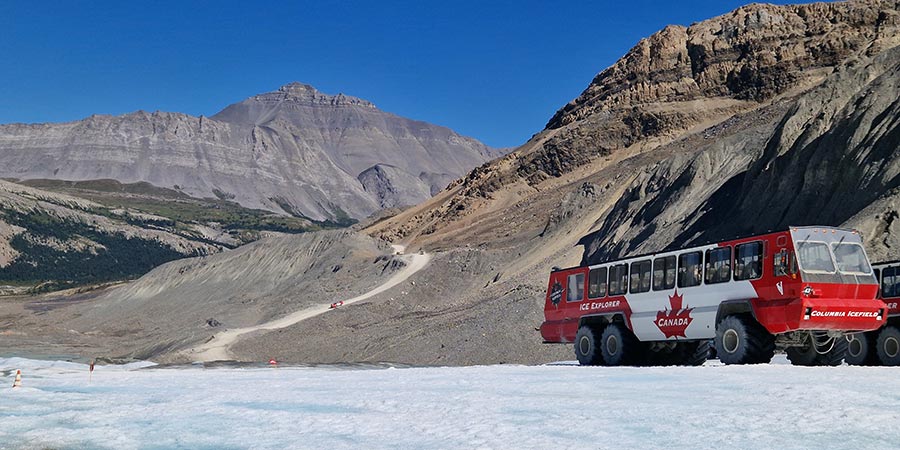 The red and white Canadian Ice Explorer bus sits on top of the frozen Icefields Parkway. 